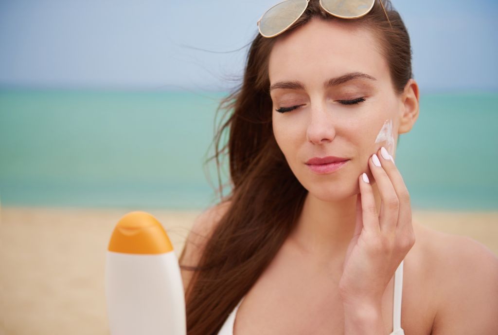 Woman applying sunscreen to protect her glowing skin from UV damage. its part of 10 must-have skincare products